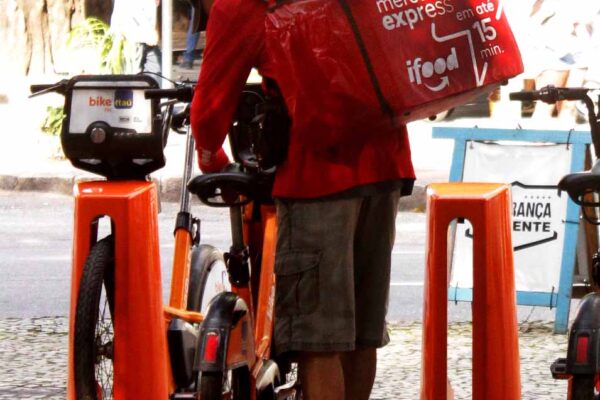 18. This worker delivers food for big national and international restaurants and supermarkets renting a bike from a big private bank without any contract, insurance or labor rights. Rio de Janeiro, Brazil, 2022.